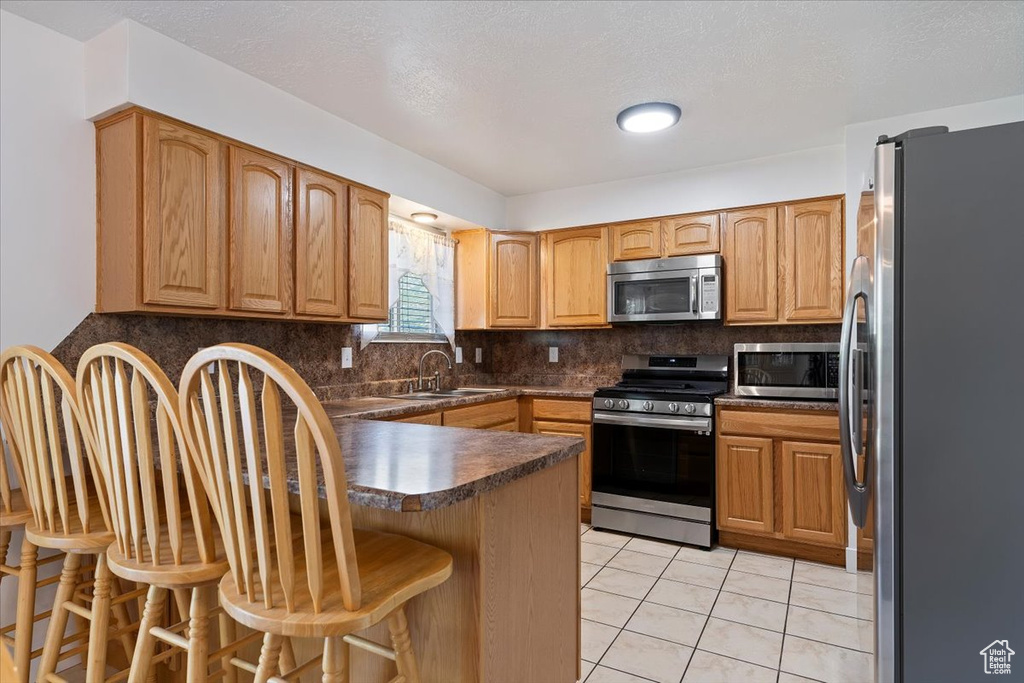 Kitchen with appliances with stainless steel finishes, a sink, a breakfast bar area, a peninsula, and tasteful backsplash