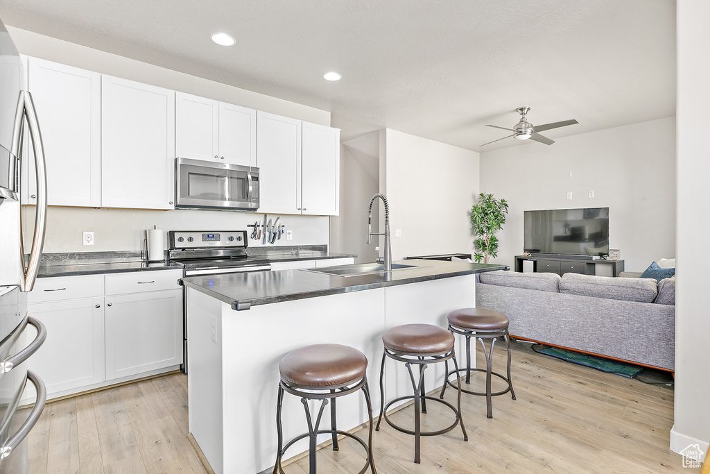Kitchen featuring stainless steel appliances, a sink, light wood-style floors, dark countertops, and a kitchen bar