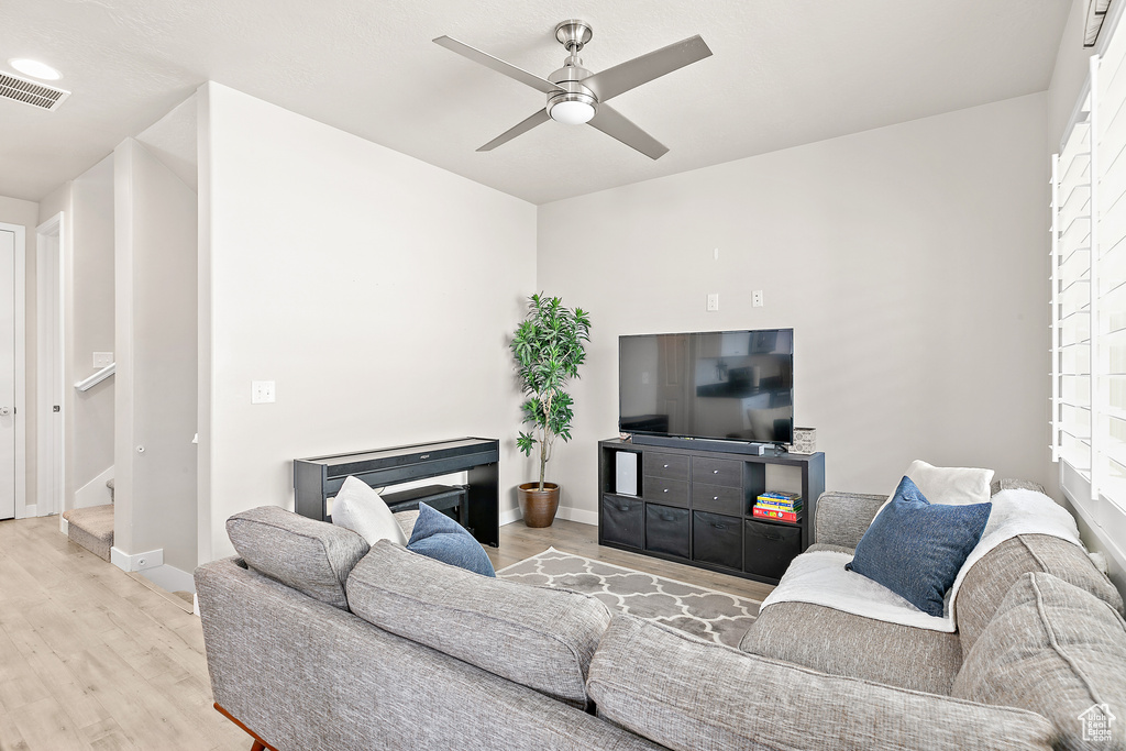 Living area with light wood finished floors, a ceiling fan, baseboards, and stairway
