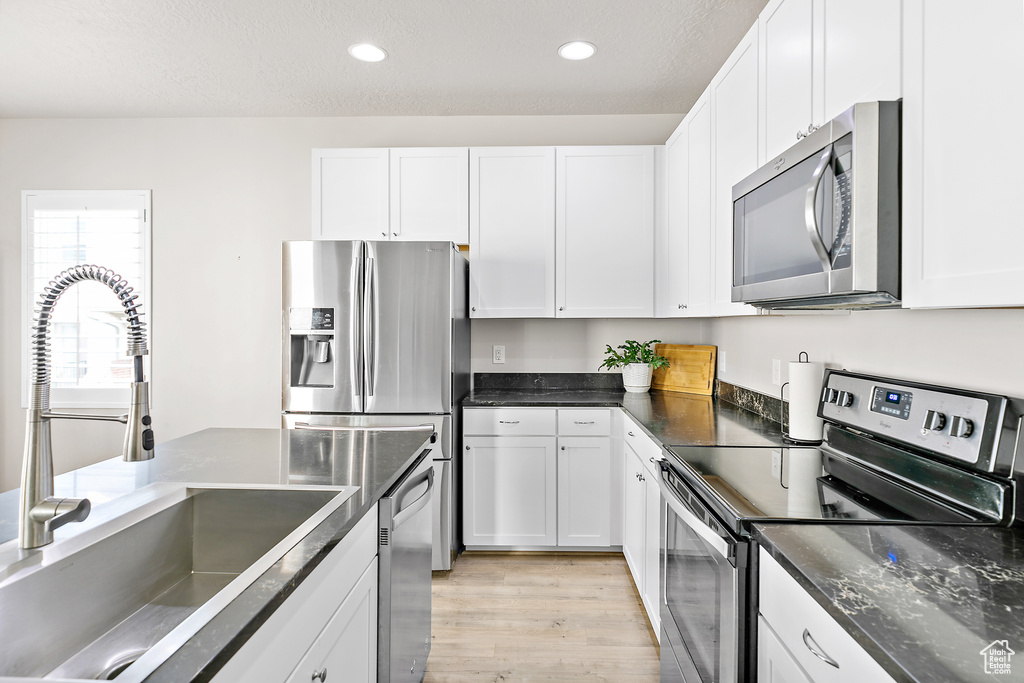 Kitchen featuring appliances with stainless steel finishes, a sink, light wood finished floors, white cabinetry, and recessed lighting