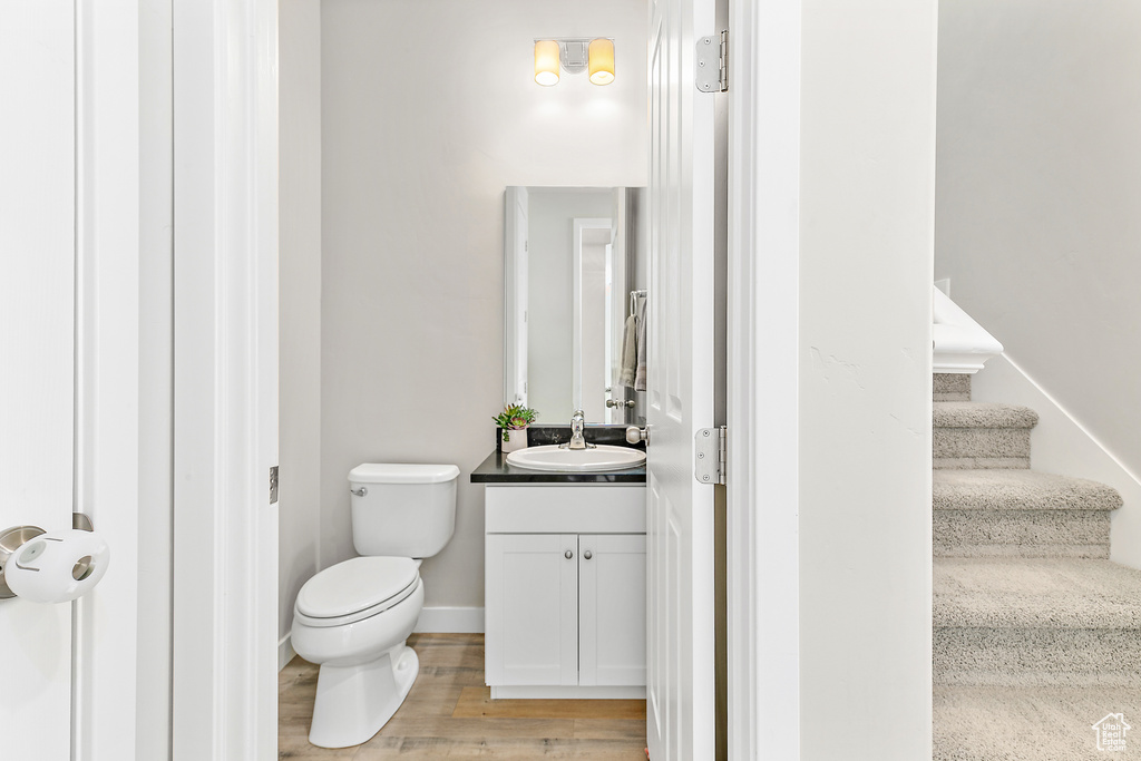 Half bath with vanity, toilet, wood finished floors, and baseboards