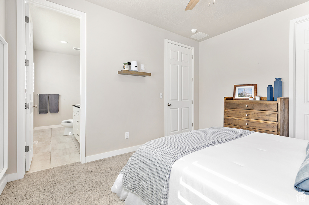 Bedroom featuring baseboards, light carpet, ensuite bathroom, and a ceiling fan