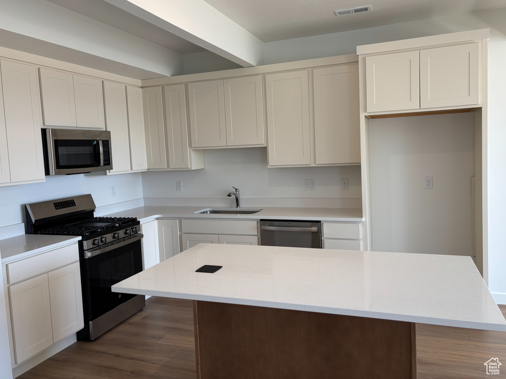 Kitchen featuring appliances with stainless steel finishes, a sink, a center island, wood finished floors, and light countertops