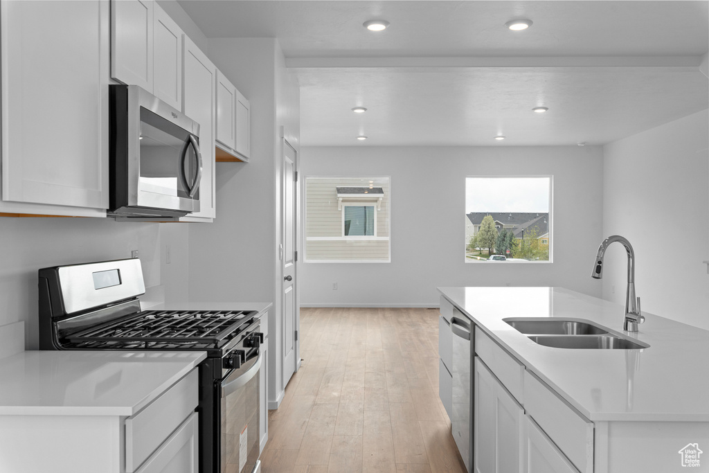 Kitchen with appliances with stainless steel finishes, a sink, light wood-style floors, light countertops, and white cabinetry