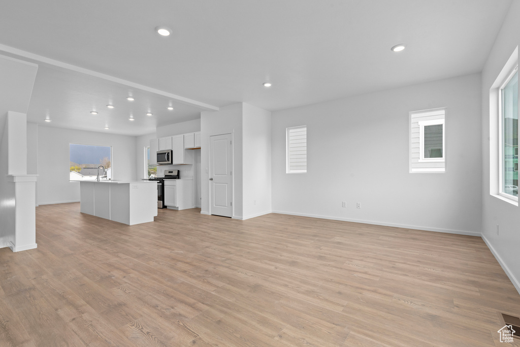 Unfurnished living room featuring light wood finished floors, recessed lighting, baseboards, and a sink