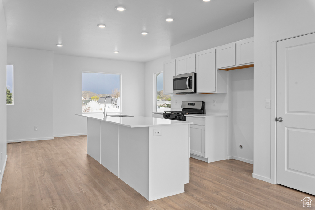 Kitchen with stainless steel appliances, a sink, recessed lighting, white cabinetry, and light wood-type flooring