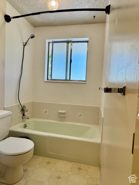Full bath with toilet, tile patterned floors, shower / washtub combination, and a textured ceiling