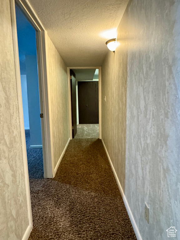 Hall with a textured ceiling, carpet, and baseboards