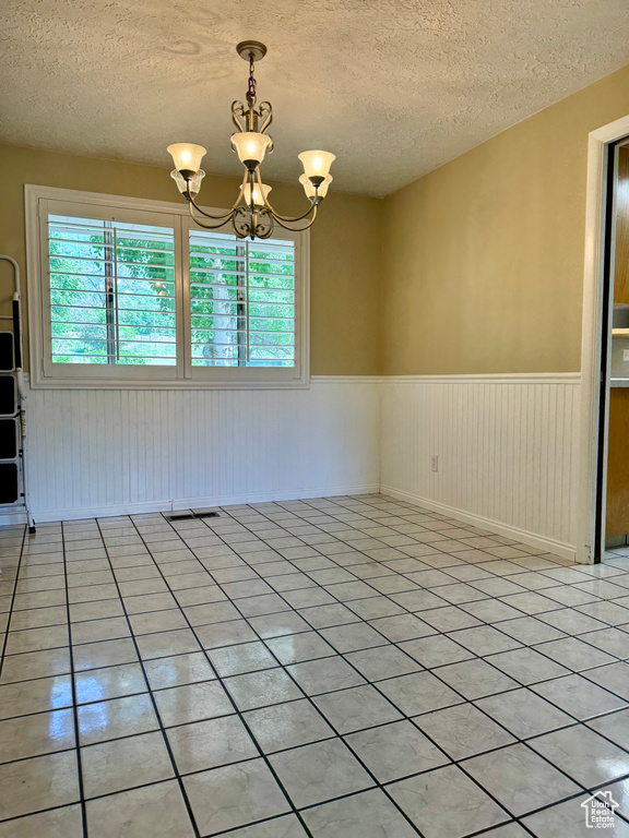 Spare room with a wainscoted wall, a textured ceiling, a chandelier, and light tile patterned flooring