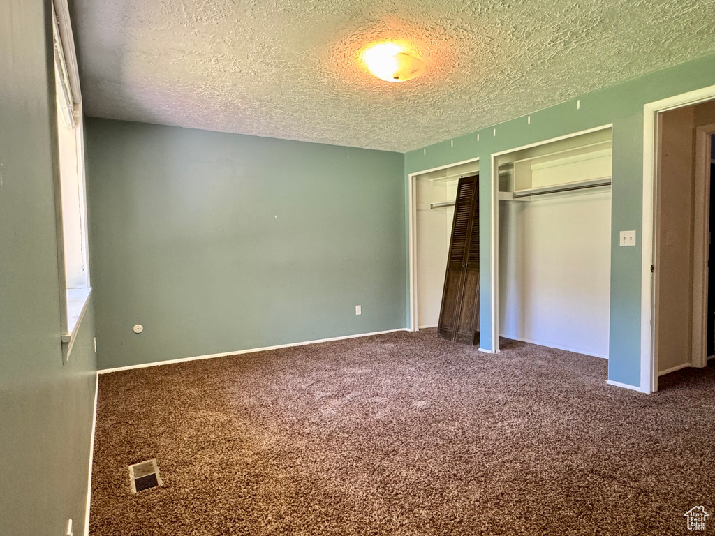 Unfurnished bedroom with a textured ceiling, two closets, carpet flooring, and baseboards