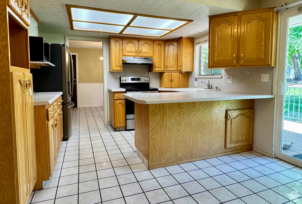 Kitchen with stainless steel appliances, under cabinet range hood, a textured ceiling, a peninsula, and light countertops