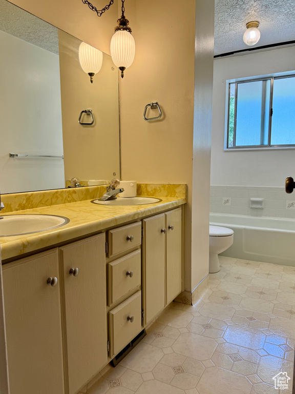 Bathroom featuring double vanity, a textured ceiling, tile patterned floors, toilet, and a bathtub