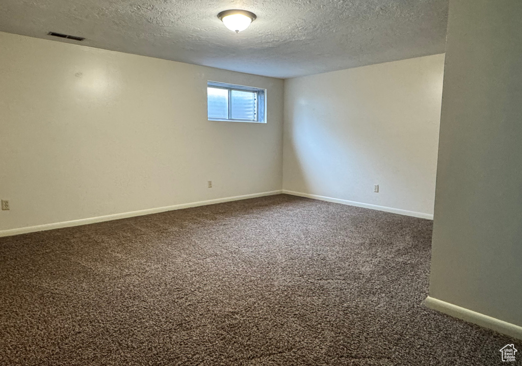 Spare room with a textured ceiling, dark carpet, and baseboards