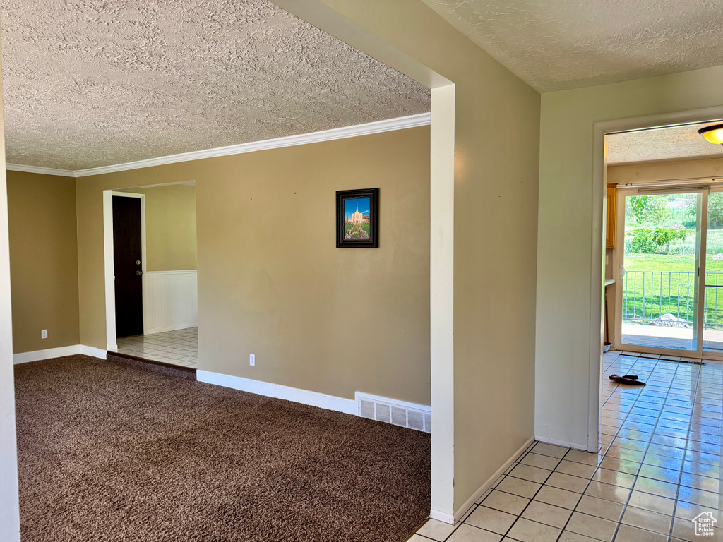 Empty room with a textured ceiling, baseboards, crown molding, and light tile patterned flooring