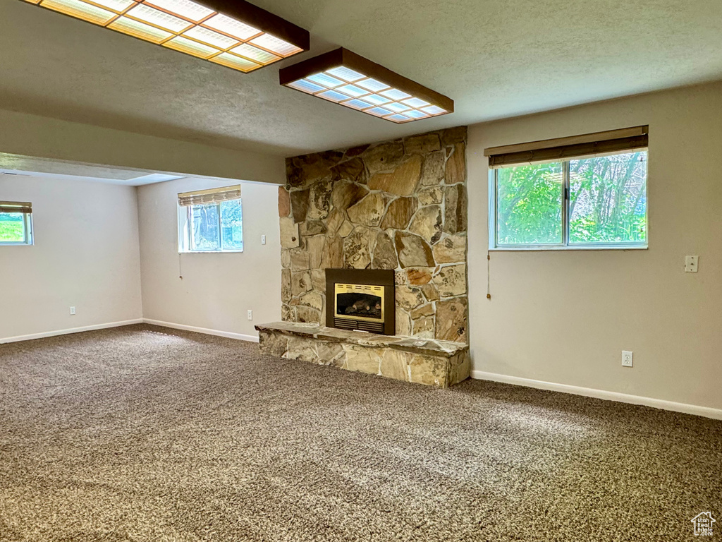 Unfurnished living room featuring carpet, a textured ceiling, a stone fireplace, and baseboards