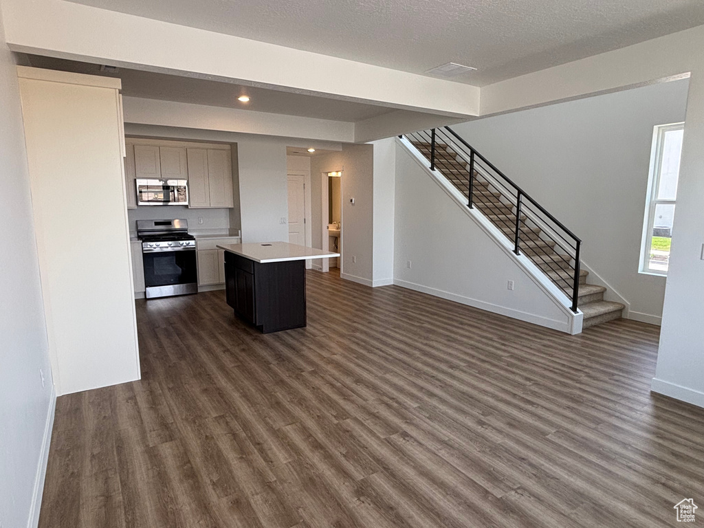 Kitchen featuring stainless steel appliances, open floor plan, dark wood-type flooring, a kitchen island, and light countertops