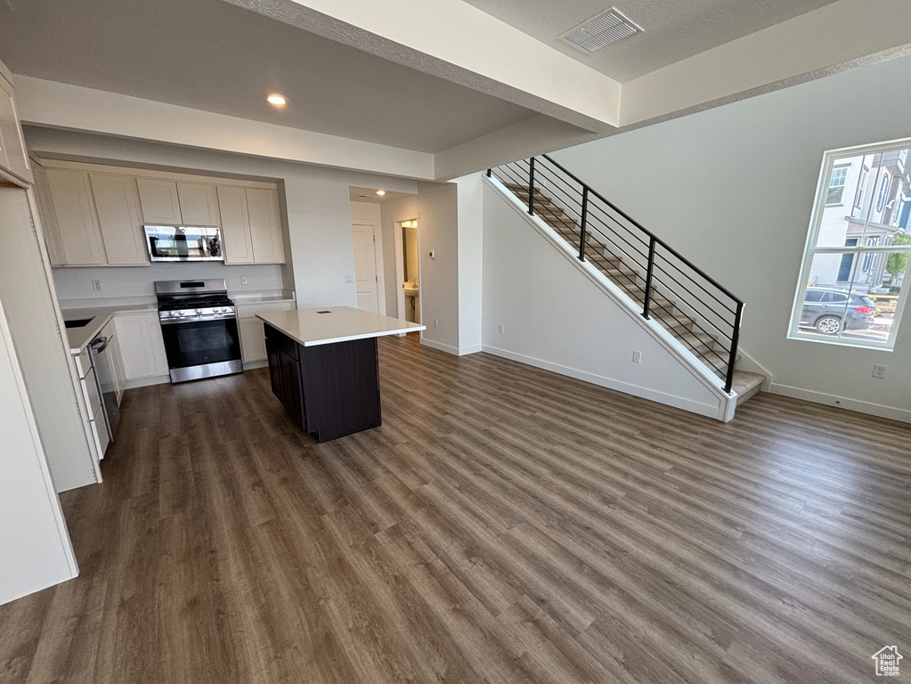 Kitchen featuring appliances with stainless steel finishes, dark wood-style floors, light countertops, a kitchen island, and baseboards