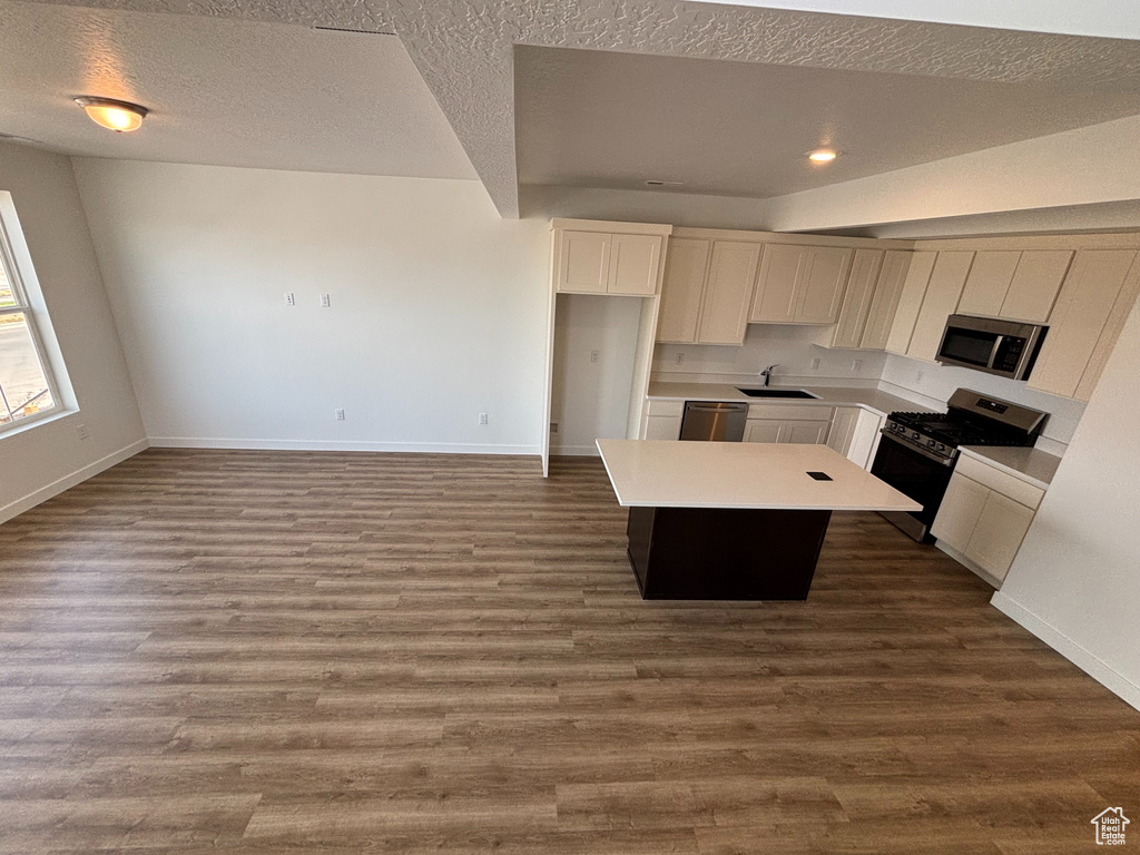 Kitchen featuring a sink, appliances with stainless steel finishes, a kitchen island, baseboards, and a textured ceiling