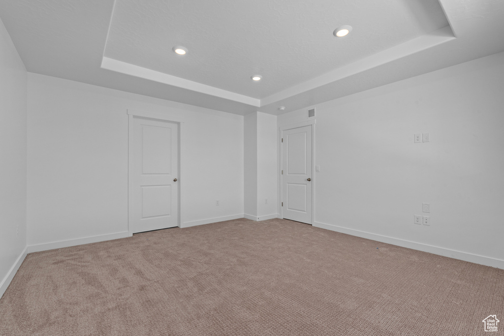 Spare room featuring a raised ceiling, recessed lighting, light carpet, and baseboards