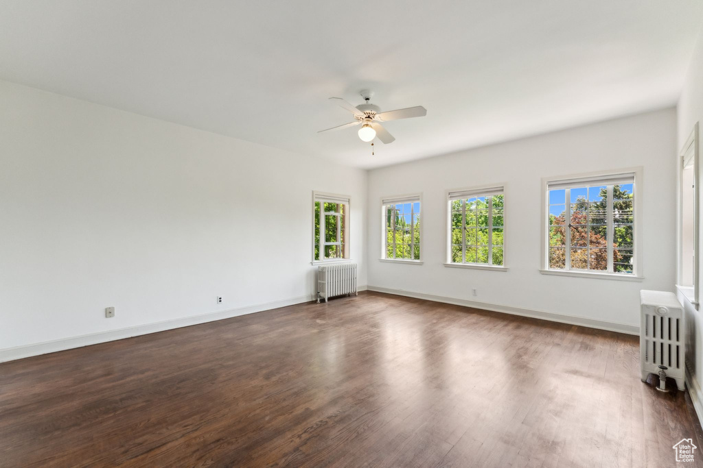 Unfurnished room with radiator heating unit, ceiling fan, dark wood-style flooring, and baseboards
