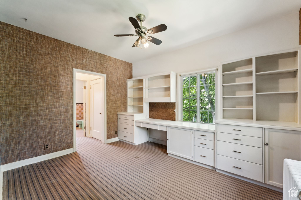 Unfurnished office with built in desk, a ceiling fan, baseboards, and carpet flooring
