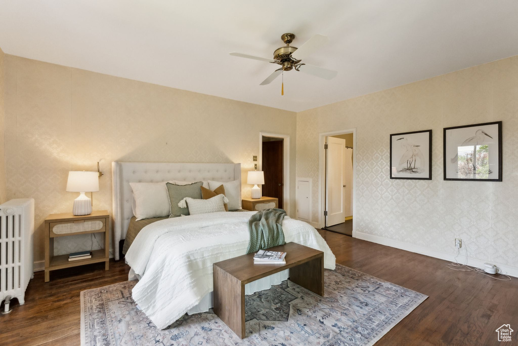 Bedroom with radiator heating unit, wood finished floors, baseboards, wallpapered walls, and ceiling fan
