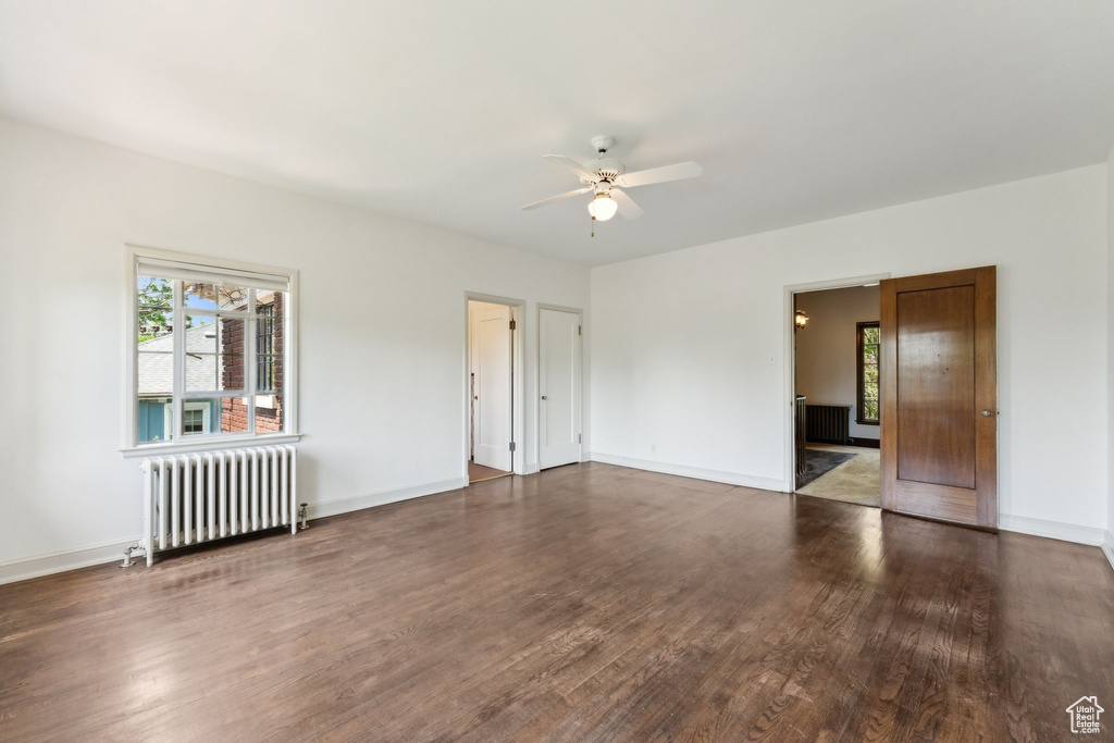 Empty room featuring radiator, a ceiling fan, wood finished floors, and baseboards