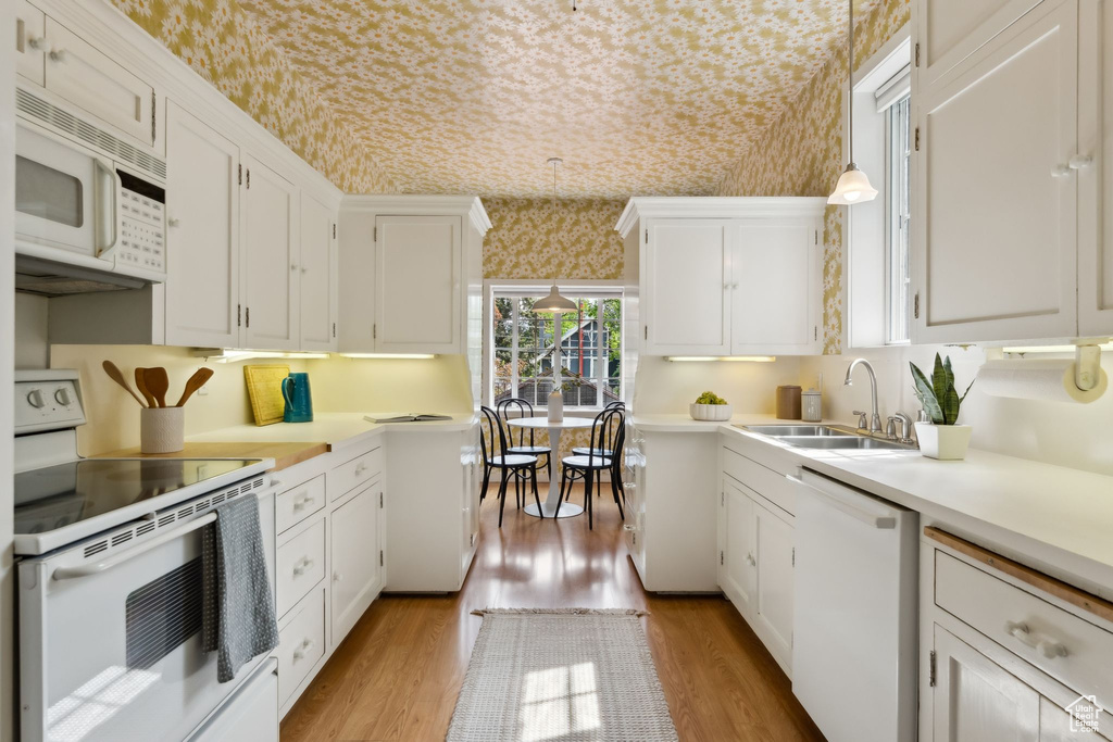 Kitchen featuring white appliances, a sink, wallpapered walls, light countertops, and light wood-style floors