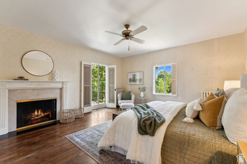 Bedroom featuring access to exterior, wood finished floors, a high end fireplace, and ceiling fan