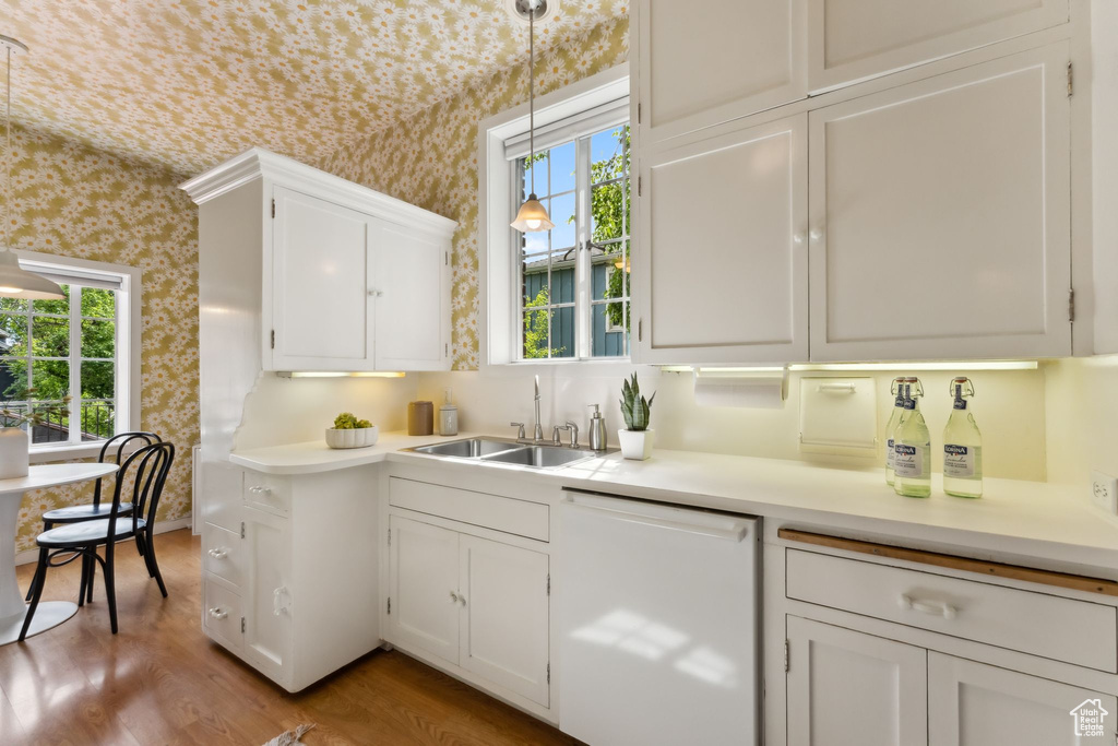 Kitchen featuring white dishwasher, a sink, wallpapered walls, white cabinets, and light countertops