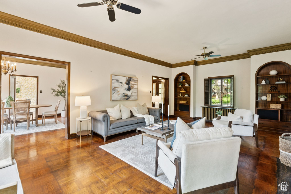 Living room featuring a ceiling fan, crown molding, a chandelier, and built in features