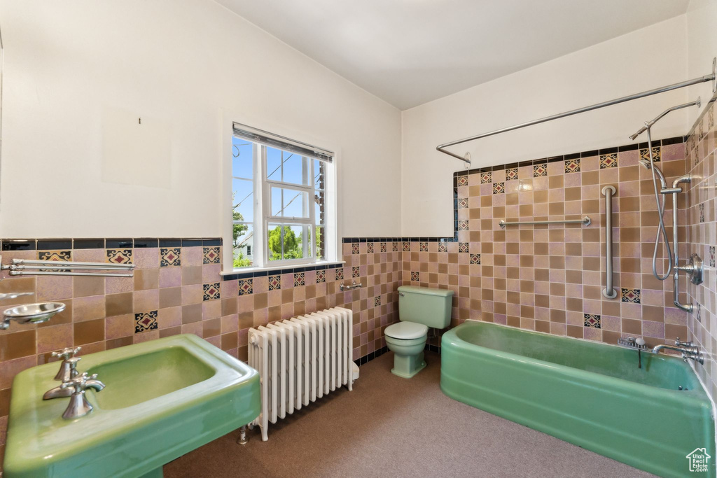 Bathroom with radiator heating unit, tile walls, toilet, wainscoting, and shower / bath combination