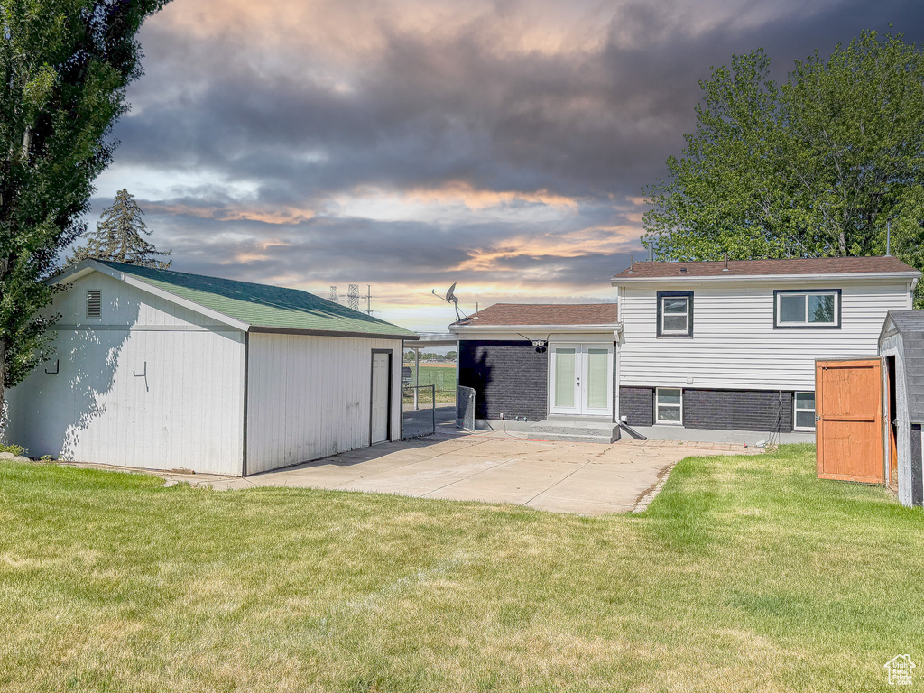 Back of property at dusk featuring french doors, a yard, an outbuilding, and a patio