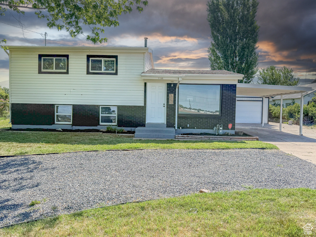 Split level home featuring concrete driveway, a front lawn, a carport, brick siding, and entry steps