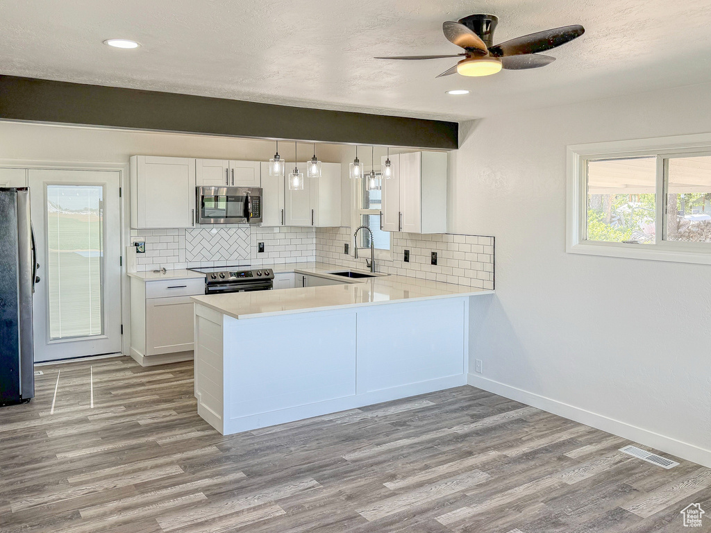 Kitchen with stainless steel appliances, light wood-style floors, decorative backsplash, light countertops, and white cabinets
