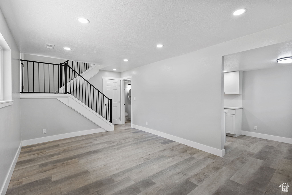 Unfurnished living room with stairs, light wood-type flooring, recessed lighting, and baseboards