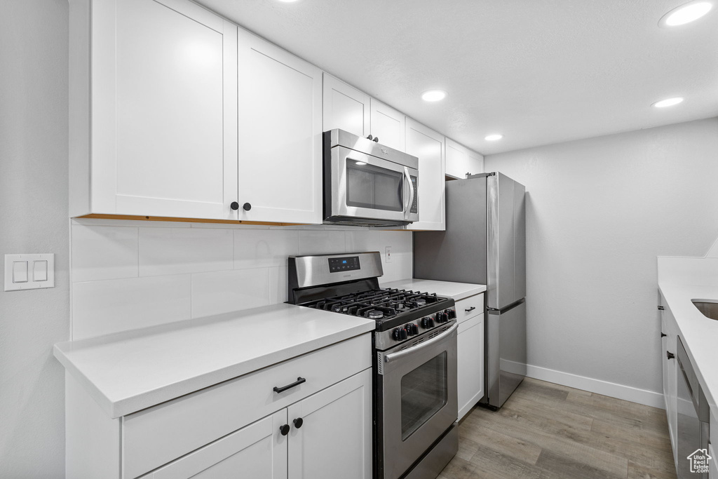 Kitchen with stainless steel appliances, light wood-style flooring, white cabinetry, baseboards, and recessed lighting