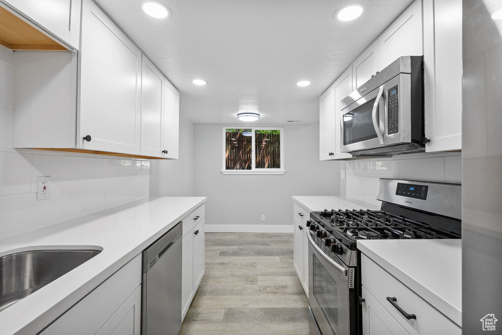 Kitchen featuring appliances with stainless steel finishes, light countertops, recessed lighting, light wood finished floors, and baseboards