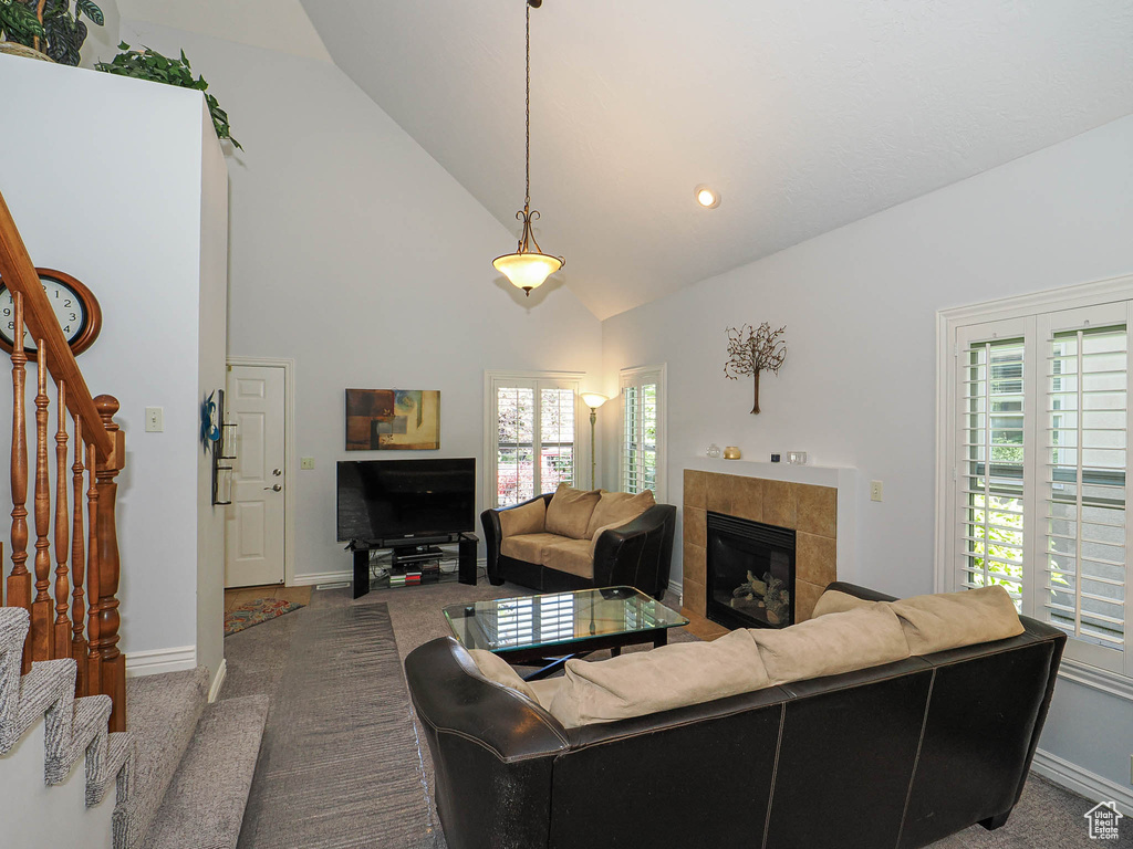 Living room featuring stairway, carpet, a tile fireplace, high vaulted ceiling, and baseboards