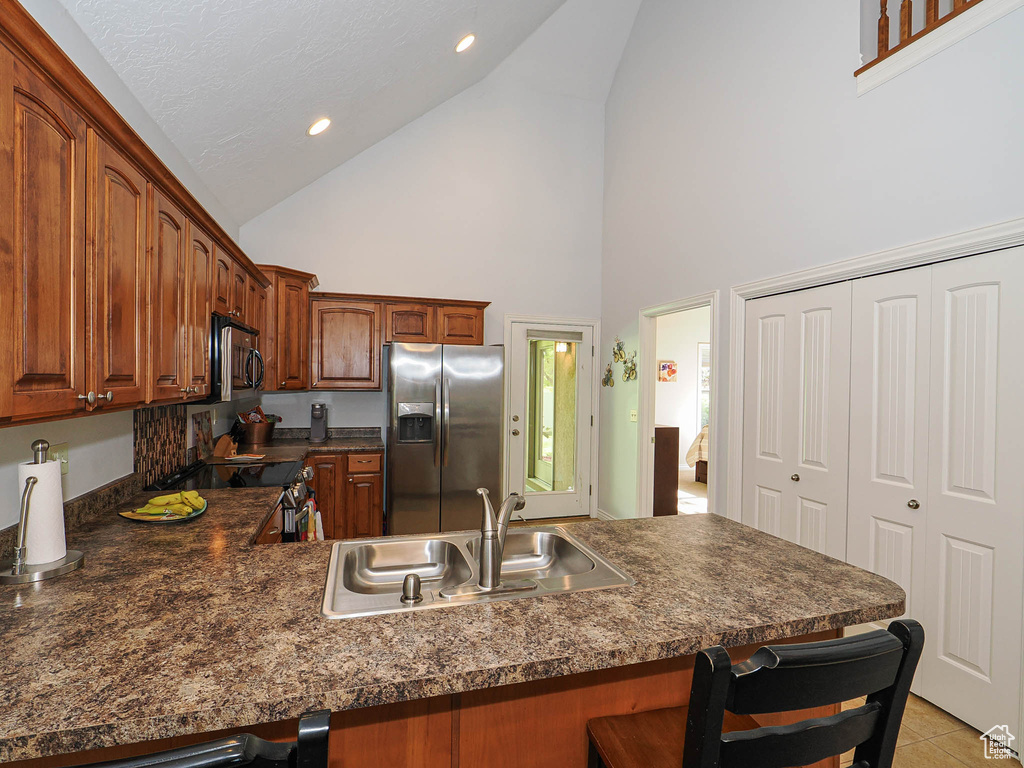 Kitchen with stainless steel appliances, a sink, high vaulted ceiling, a kitchen bar, and dark countertops