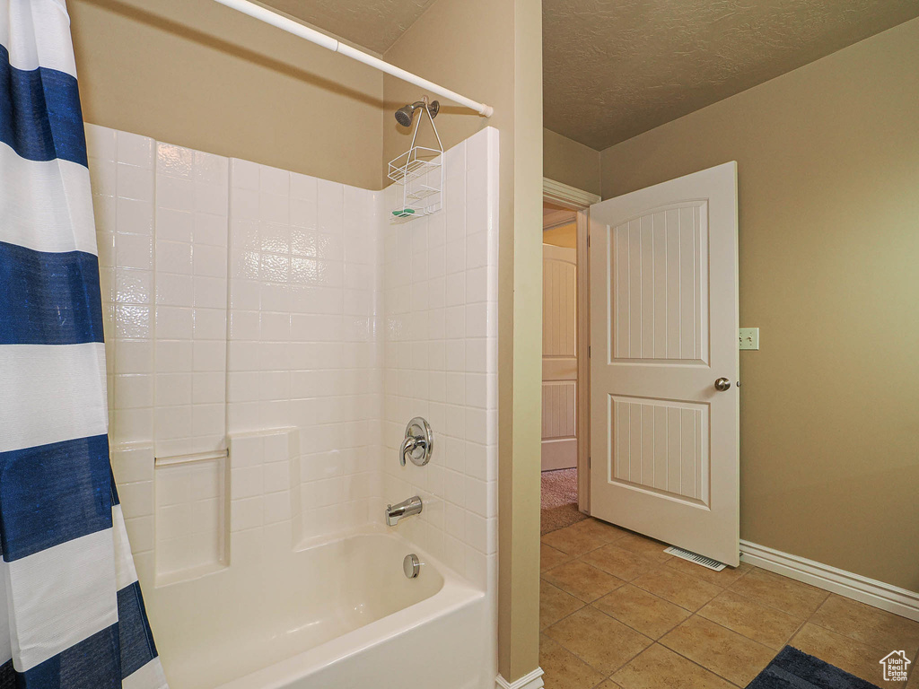 Full bath featuring shower / bath combo, tile patterned floors, baseboards, and a textured ceiling