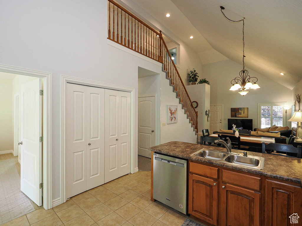 Kitchen with stainless steel dishwasher, a sink, high vaulted ceiling, dark countertops, and a chandelier