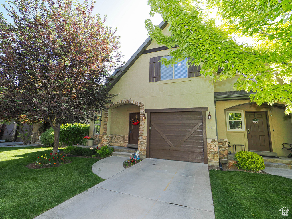 Tudor-style house featuring stucco siding, driveway, an attached garage, stone siding, and a front yard