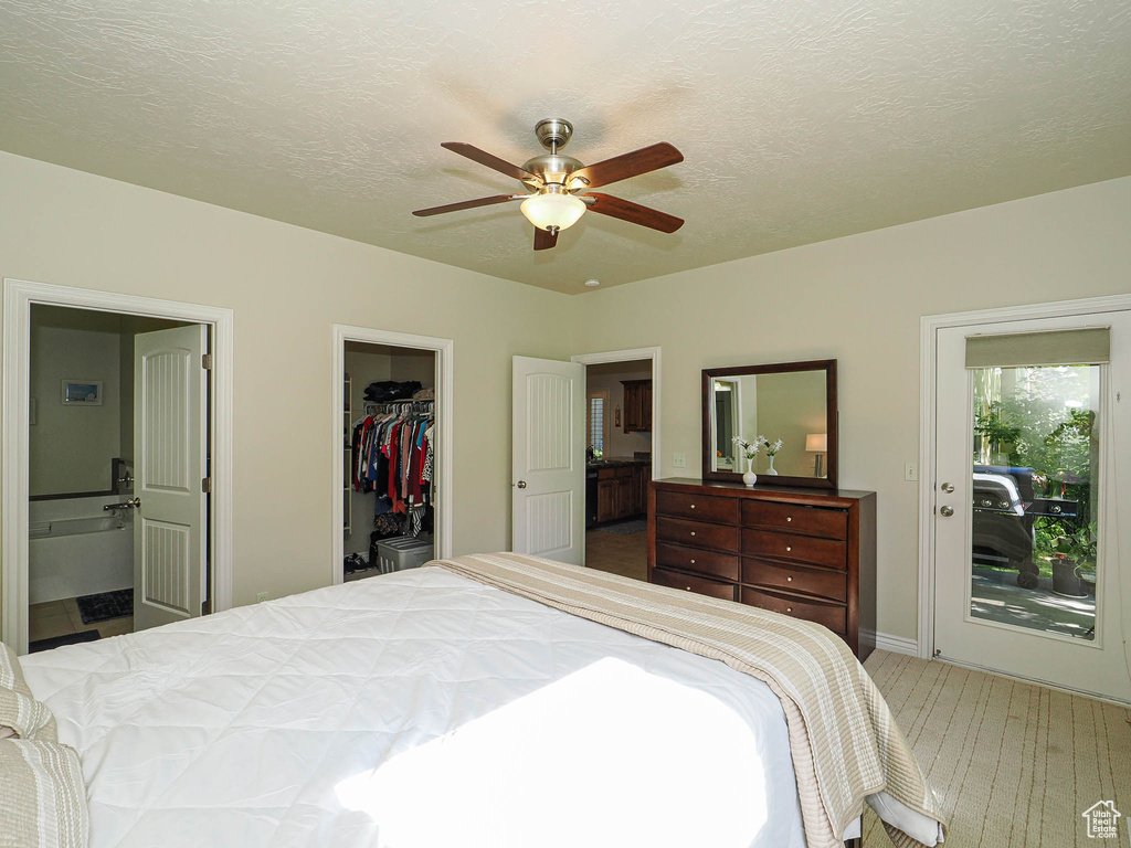 Carpeted bedroom featuring a walk in closet, a closet, connected bathroom, a textured ceiling, and a ceiling fan