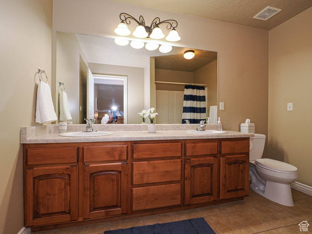 Bathroom featuring double vanity, toilet, tile patterned floors, a shower with shower curtain, and baseboards