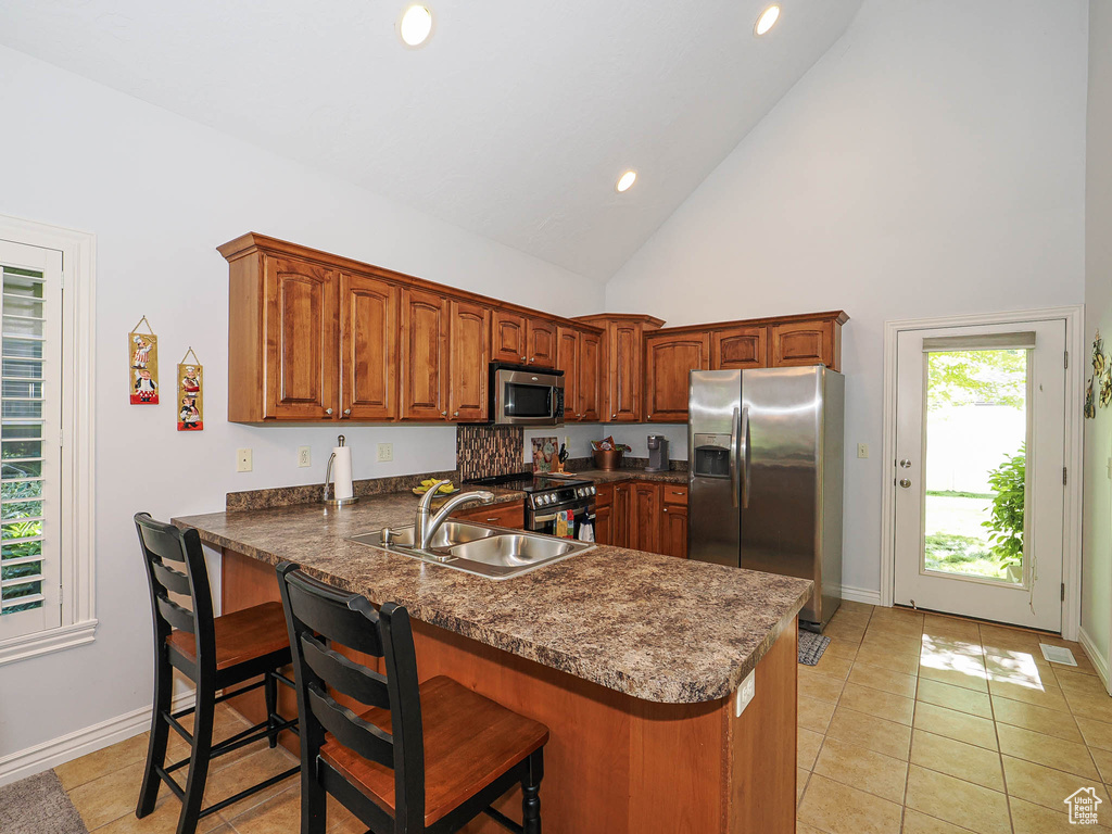 Kitchen featuring appliances with stainless steel finishes, a peninsula, dark countertops, high vaulted ceiling, and a breakfast bar