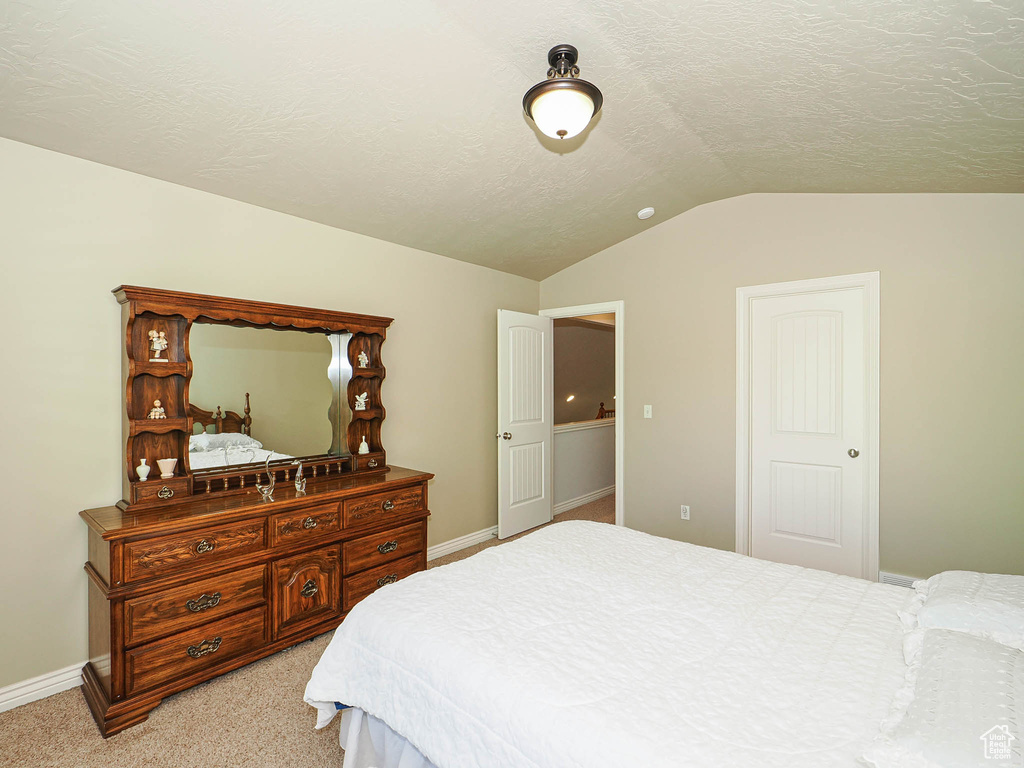 Bedroom with lofted ceiling, baseboards, light colored carpet, and a textured ceiling