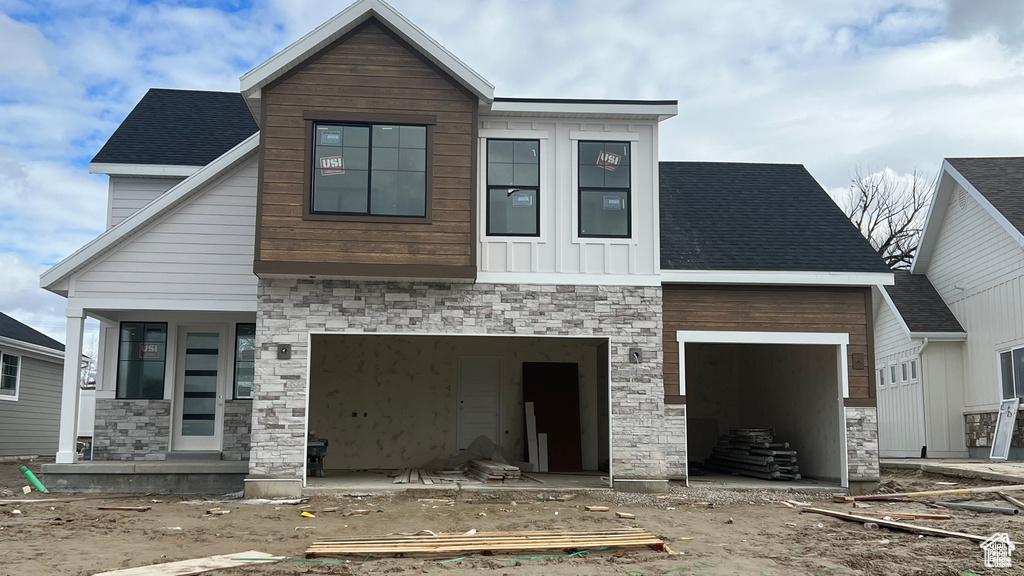 Modern home with stone siding, an attached garage, and roof with shingles