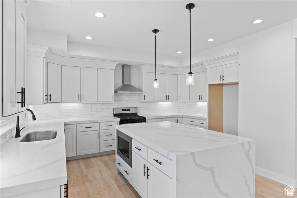 Kitchen featuring wall chimney range hood, stainless steel appliances, a sink, a kitchen island, and decorative backsplash