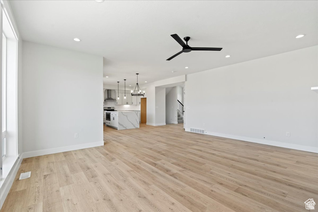 Unfurnished living room featuring ceiling fan, recessed lighting, light wood-style flooring, baseboards, and a chandelier